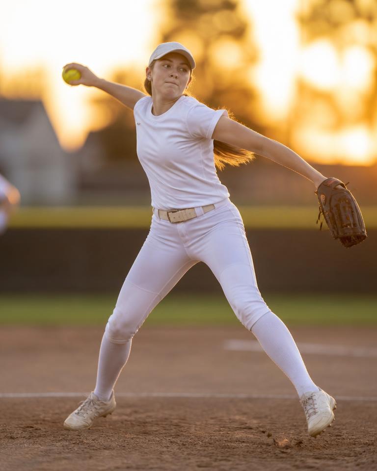 Youth softball pitcher throwing at sunset